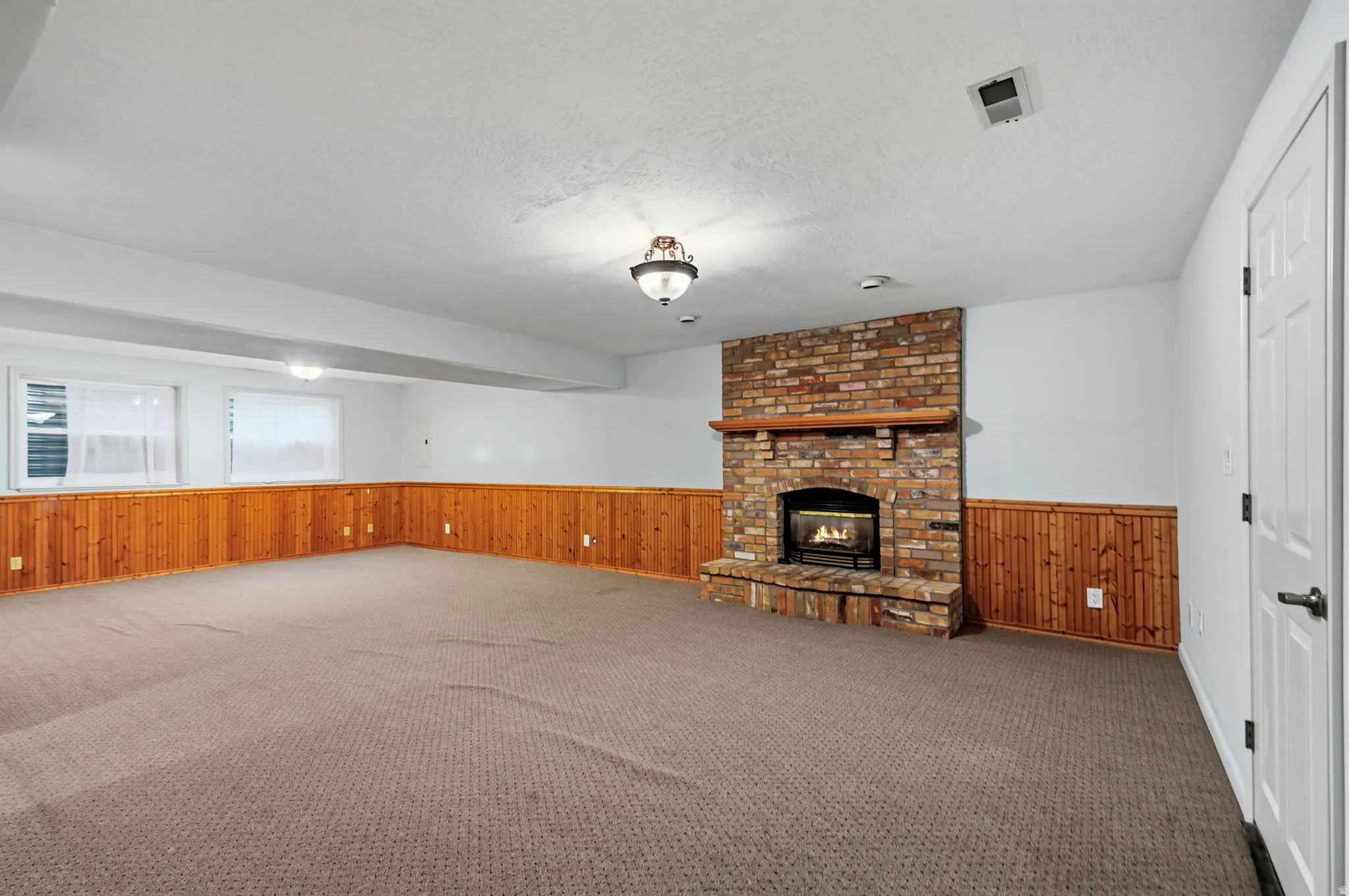 Spacious room featuring a corner brick fireplace with a wood mantle, wood paneling, and carpeted flooring