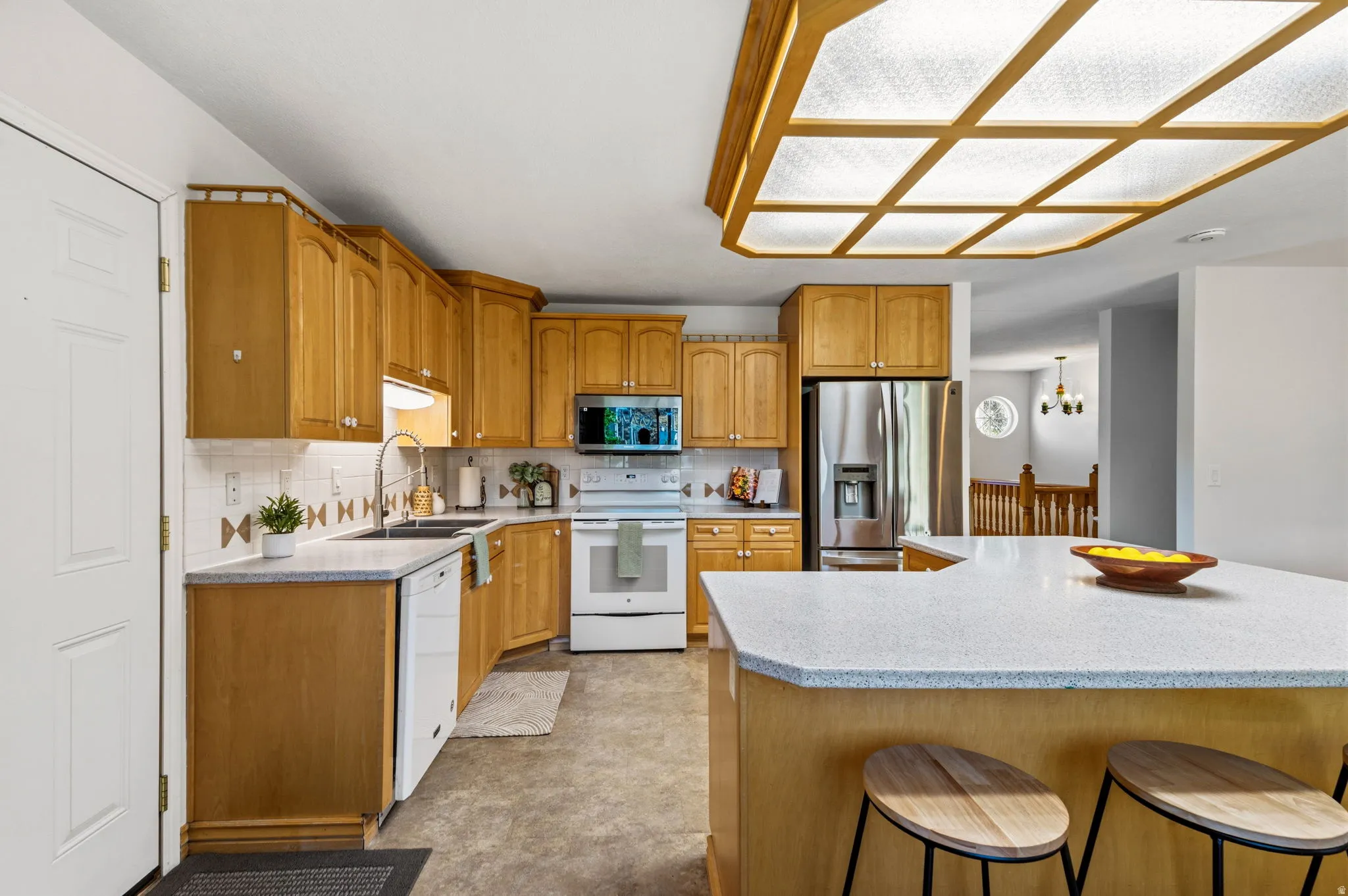 Kitchen featuring light wood cabinetry, stainless steel refrigerator, white appliances, solid surface countertops, and a full tile backsplash