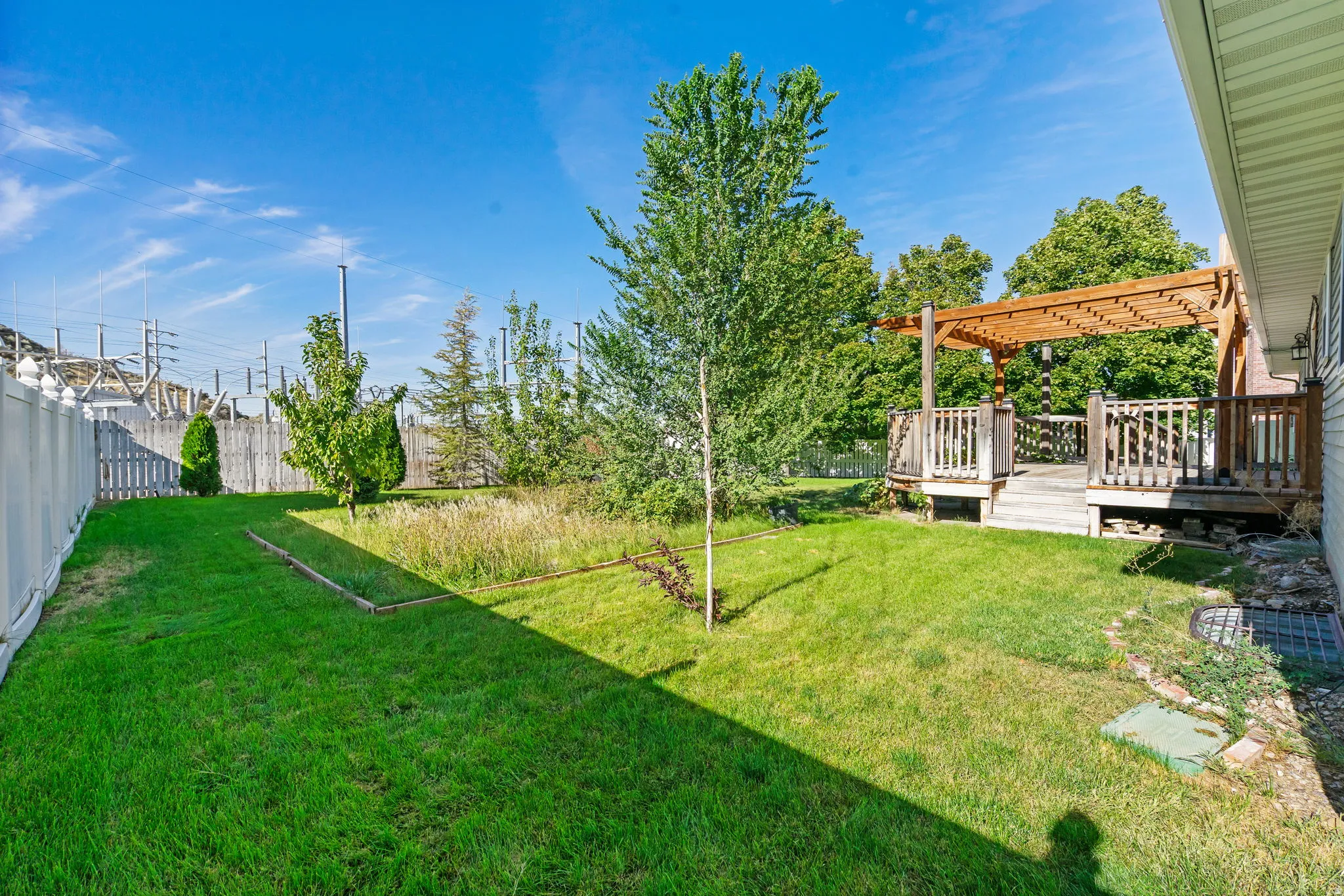 Wood deck with pergola, expansive green lawn, white privacy fencing, and mature trees