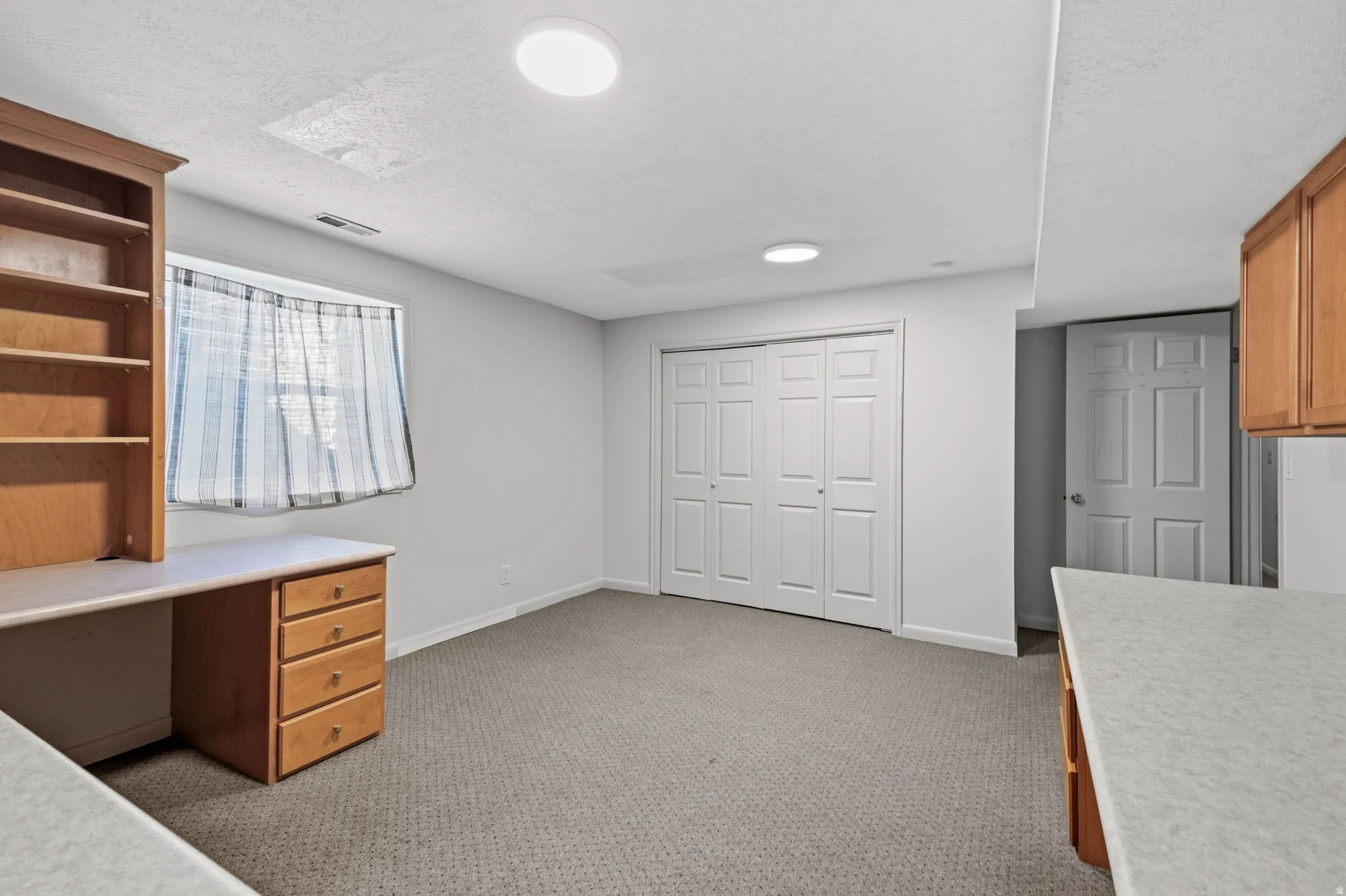 Recessed lighting, wood-finish built-in desk with shelving, light-colored carpeting, window with natural light, and bi-fold closet doors