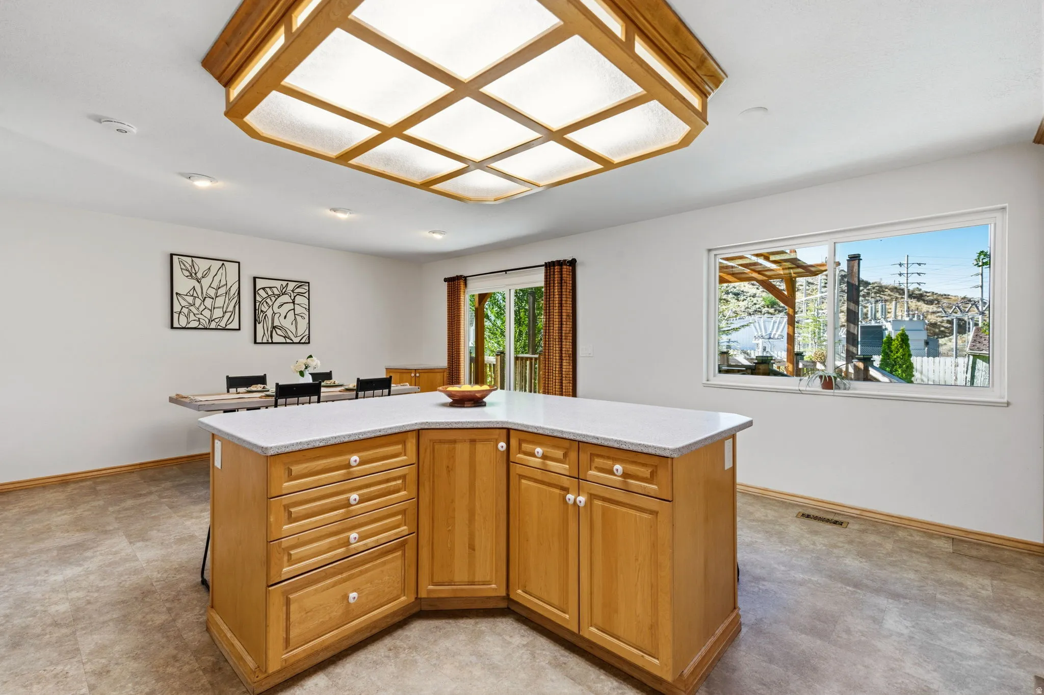 Kitchen island with light wood cabinetry and light-toned countertop, recessed lighting, and a large ceiling-mounted light fixture
