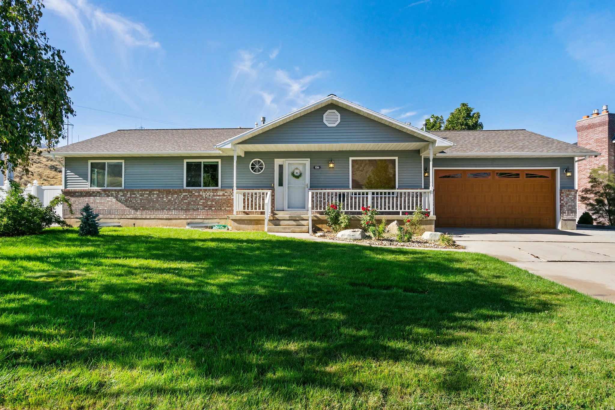 Exterior featuring gray siding, a wood-finish garage door, white porch railing, and a manicured lawn