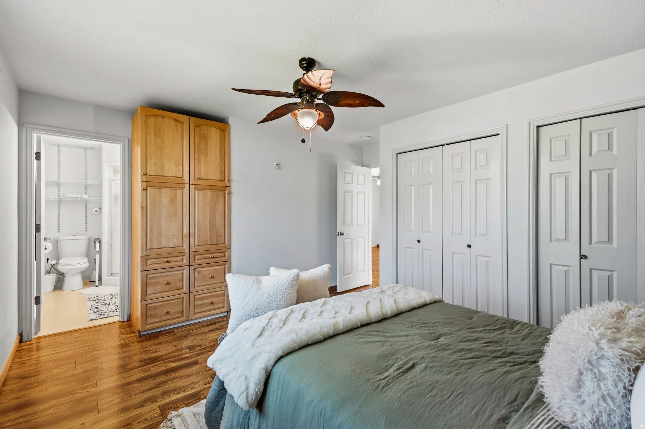 Wood-finish flooring, built-in wooden cabinetry, ceiling fan, and two white bi-fold closet doors