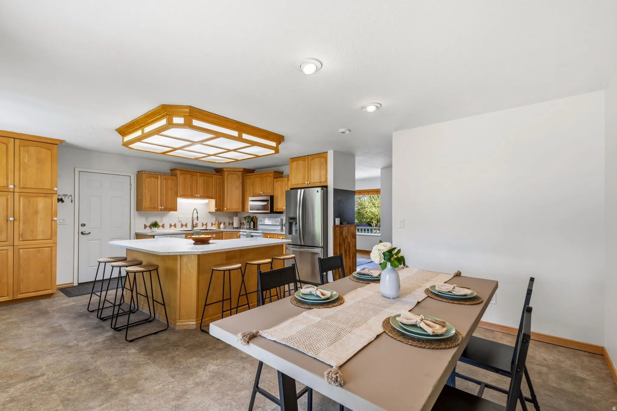 Kitchen featuring light wood cabinetry, a central island with countertop seating, stainless steel appliances, and a tiled backsplash