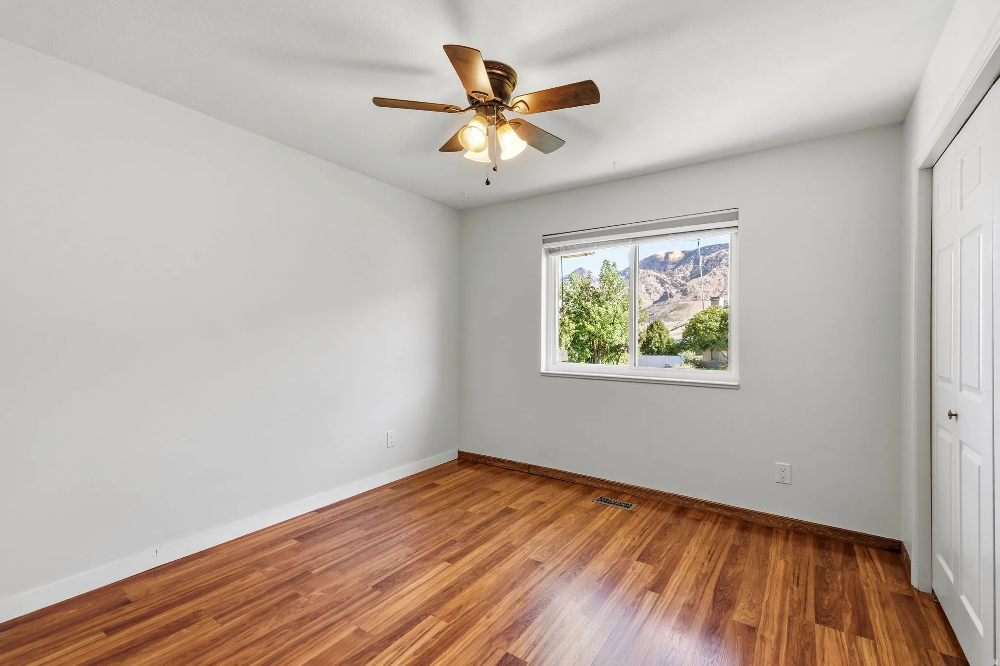 Wood-finish flooring, ceiling fan with integrated lighting, a window showcasing a mountain landscape, and a bi-fold closet door
