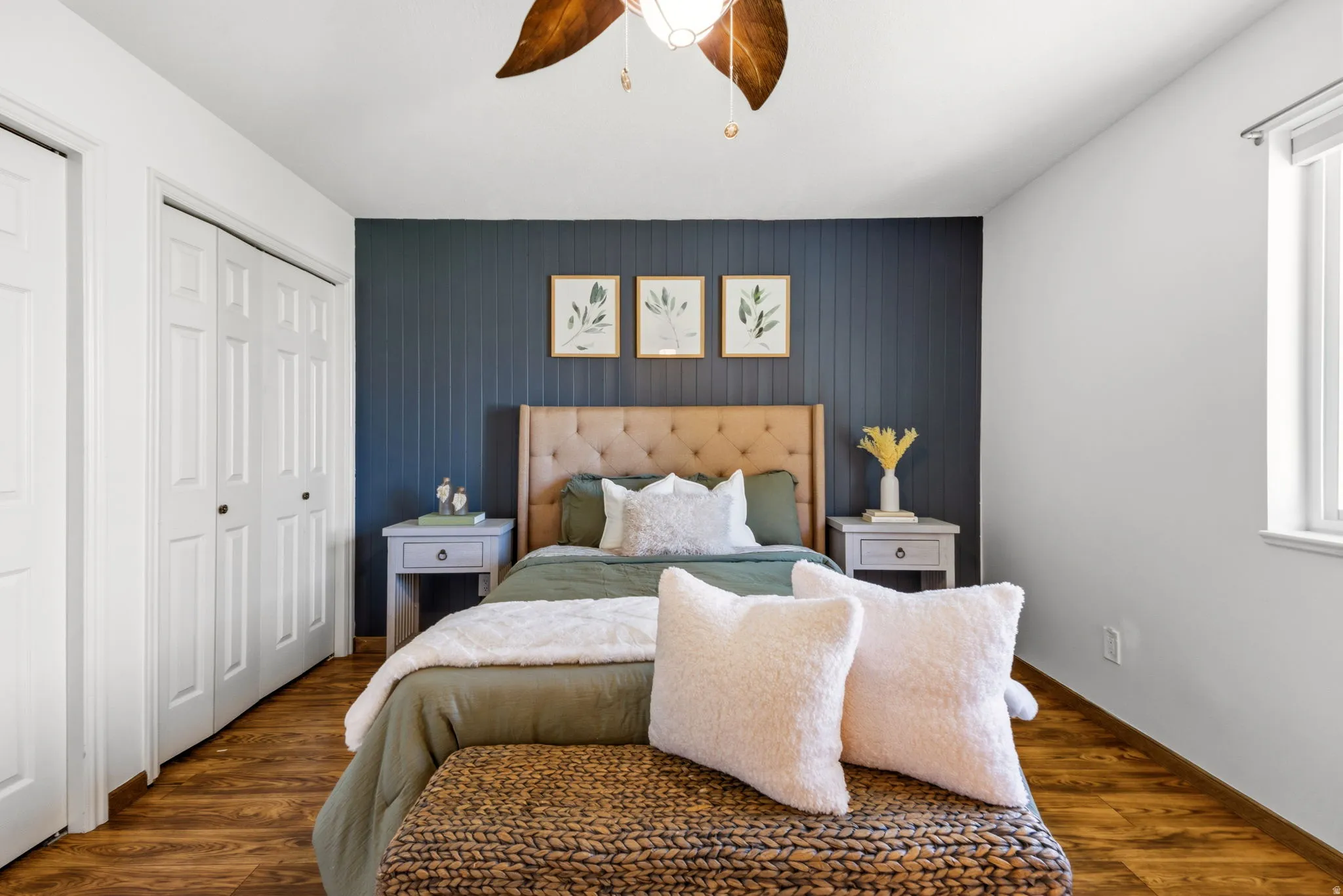 Bedroom featuring wood-finish flooring, a decorative accent wall, a ceiling fan with light fixture, and a window with vertical blinds