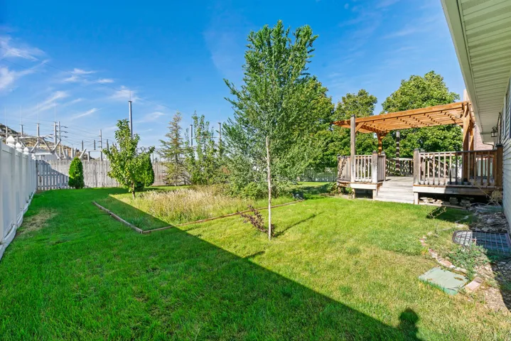 Wood deck with pergola, expansive green lawn, white privacy fencing, and mature trees