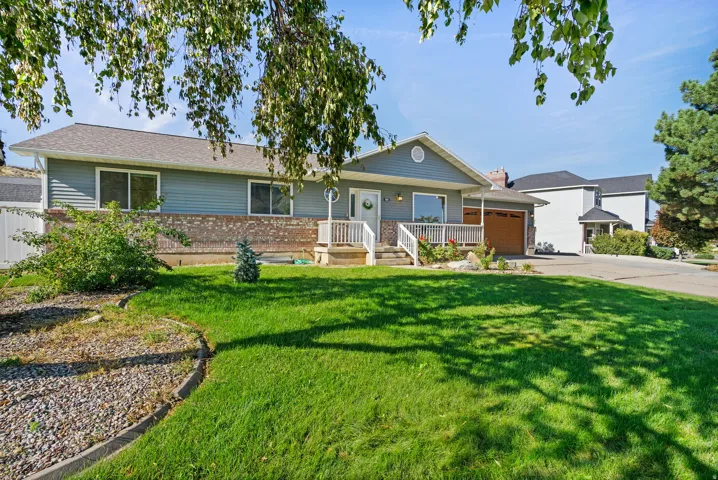 Light blue siding exterior with brick accents, covered front porch, white railings, attached garage with wood-finish door, and a manicured lawn