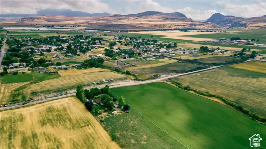 Expansive rural landscape featuring a mix of green and golden fields, distant mountains, and a community of homes
