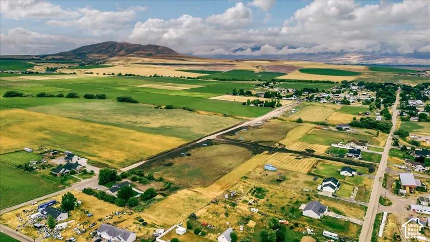 Expansive rural landscape featuring a mountainous backdrop, varied agricultural fields, and a residential area with single-story homes