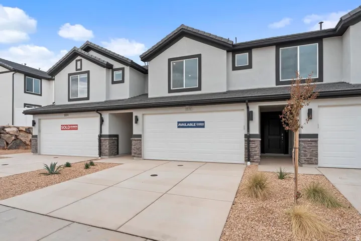 Contemporary exterior with a smooth stucco finish and dark trim, featuring an integrated garage, stone veneer accents, and a paved driveway
