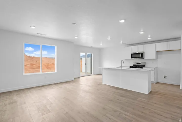 Open-concept living space featuring wood-finish flooring, recessed lighting, and a kitchen with white cabinetry and stainless steel appliances