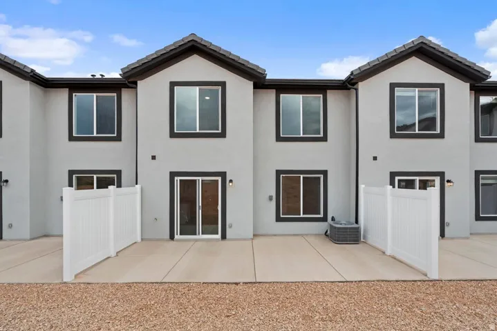 Rear exterior featuring light stucco, dark trim, a concrete patio, white privacy fencing, and sliding glass doors