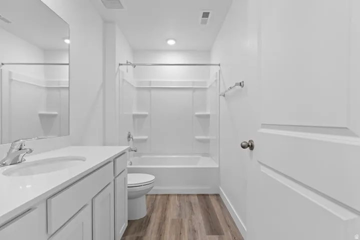 Contemporary bathroom featuring a white vanity with integrated sink, chrome faucet, wood-finish flooring, and a white tub with shower surround