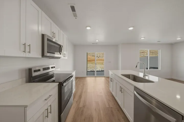 Kitchen featuring white cabinetry, stainless steel appliances, light-toned countertops, wood-finish flooring, and recessed lighting