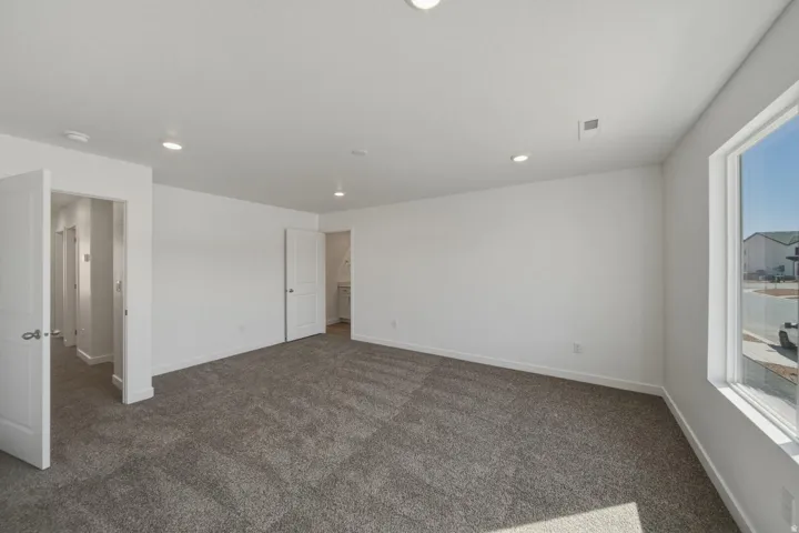 Spacious room featuring neutral carpeting, white painted walls, recessed lighting, and ample natural light from a large window