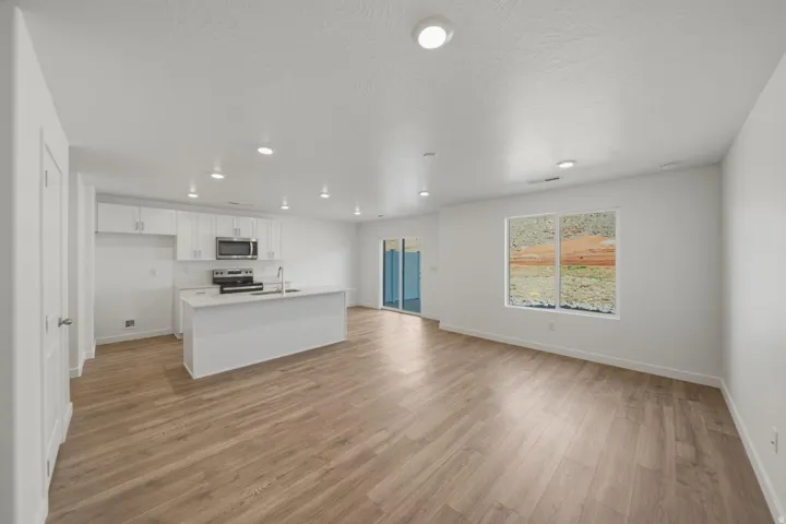 Open-concept living space with wood-finish flooring, recessed lighting, and a kitchen featuring white cabinetry and stainless steel appliances