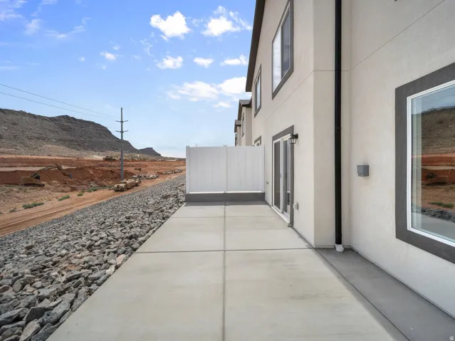 Rear concrete patio with a white privacy fence, exterior light fixture, and sliding glass door