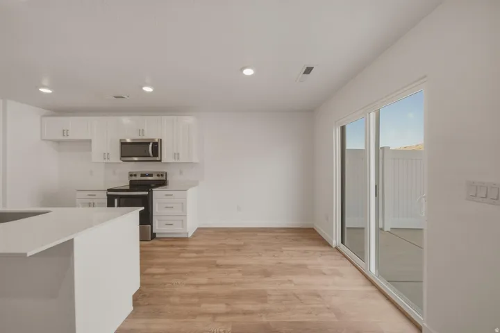 Modern kitchen with white cabinetry, stainless steel appliances, wood-finish flooring, recessed lighting, and a sliding glass door to an outdoor patio