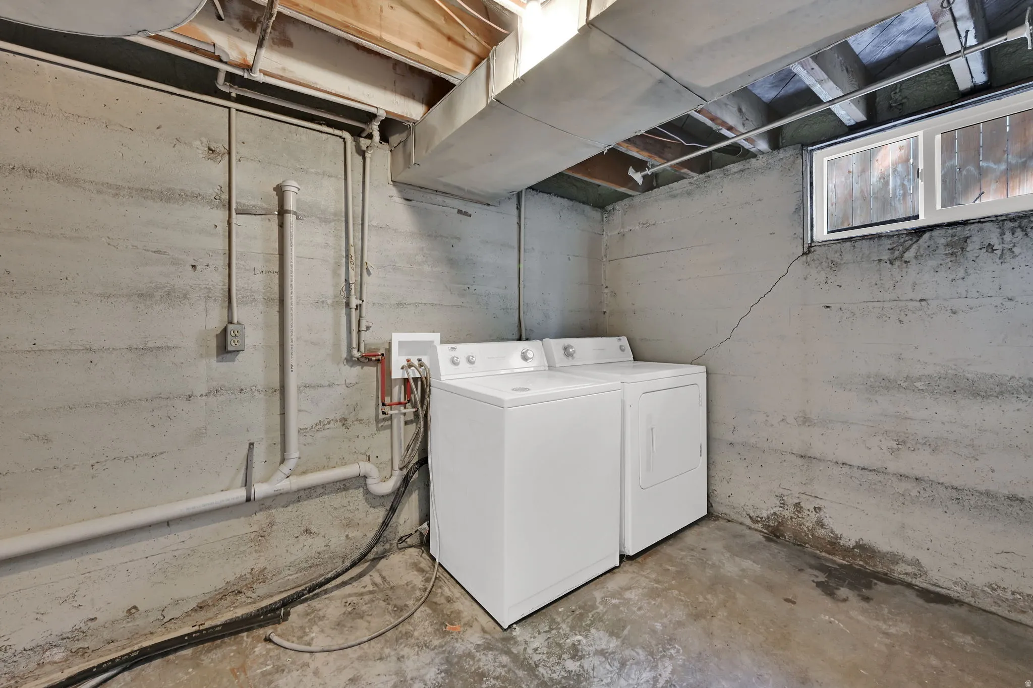 Utility space with exposed concrete walls, exposed wood ceiling joists, and a window