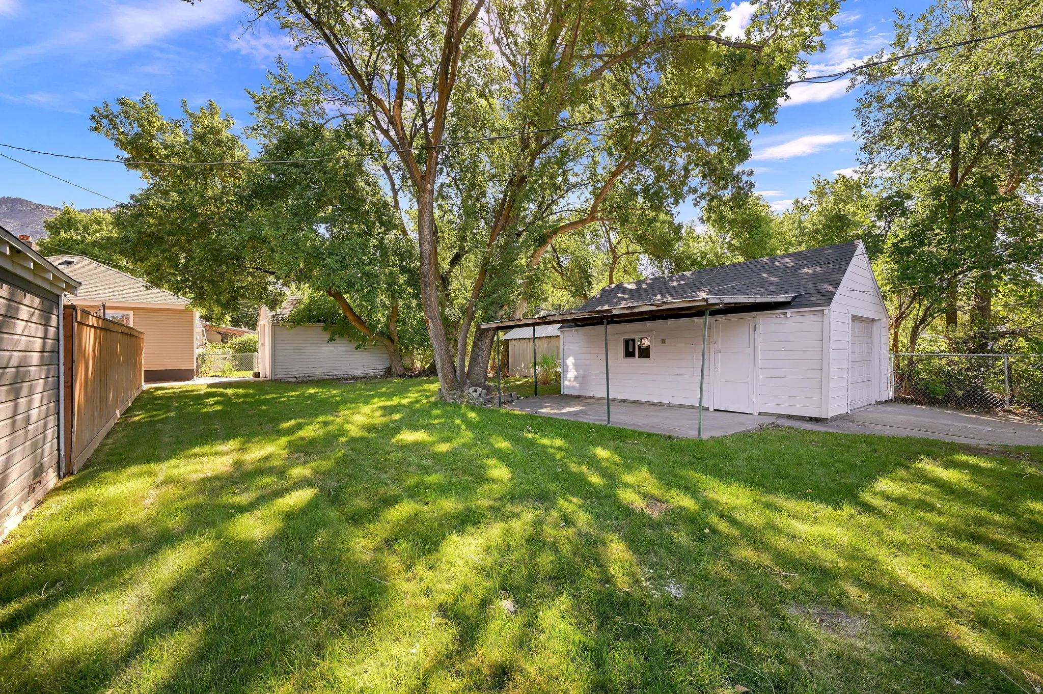 Expansive grassy yard with mature trees, a detached white garage structure, and a covered patio area