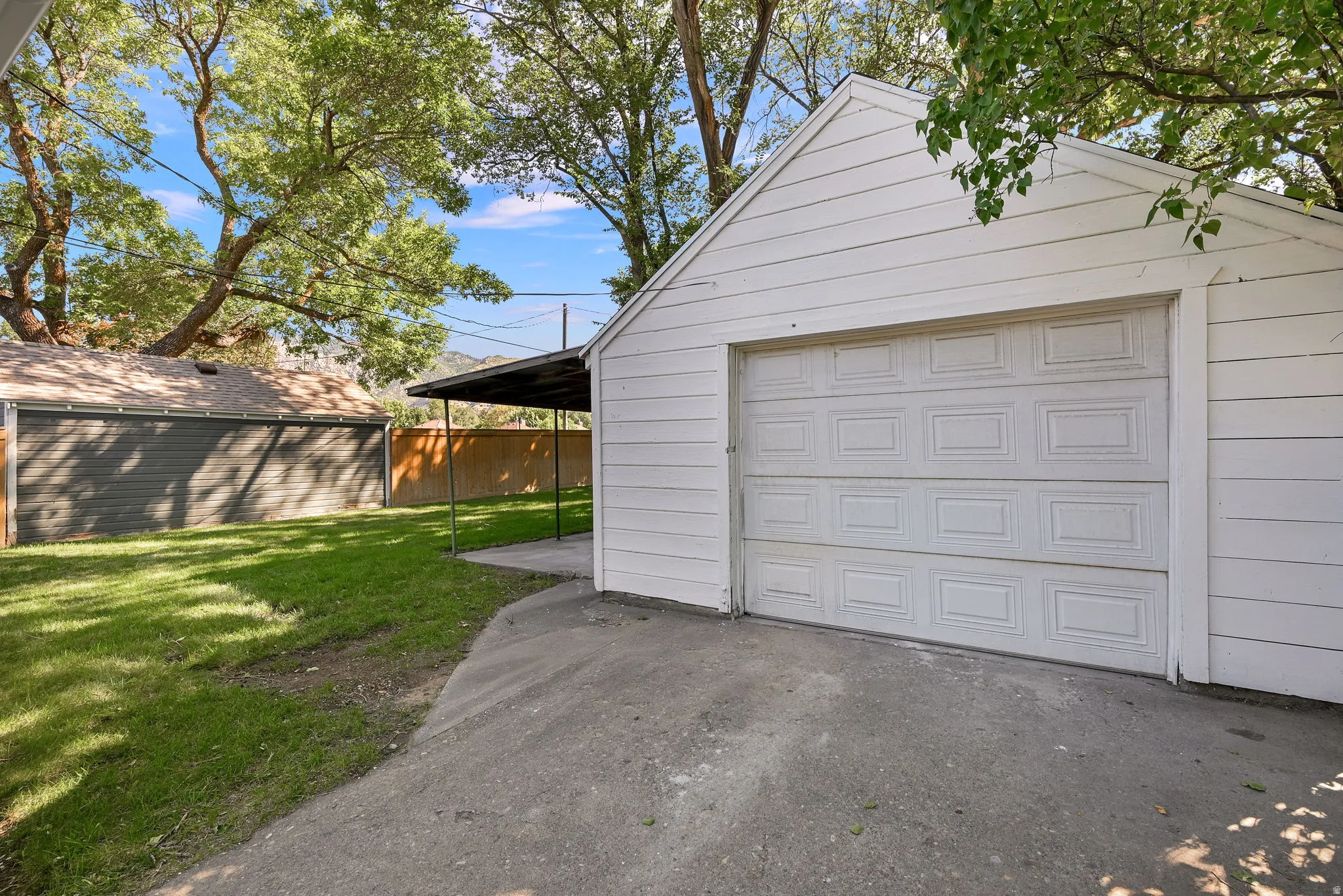 Attached single-car garage with a panel door, concrete driveway, and covered patio area