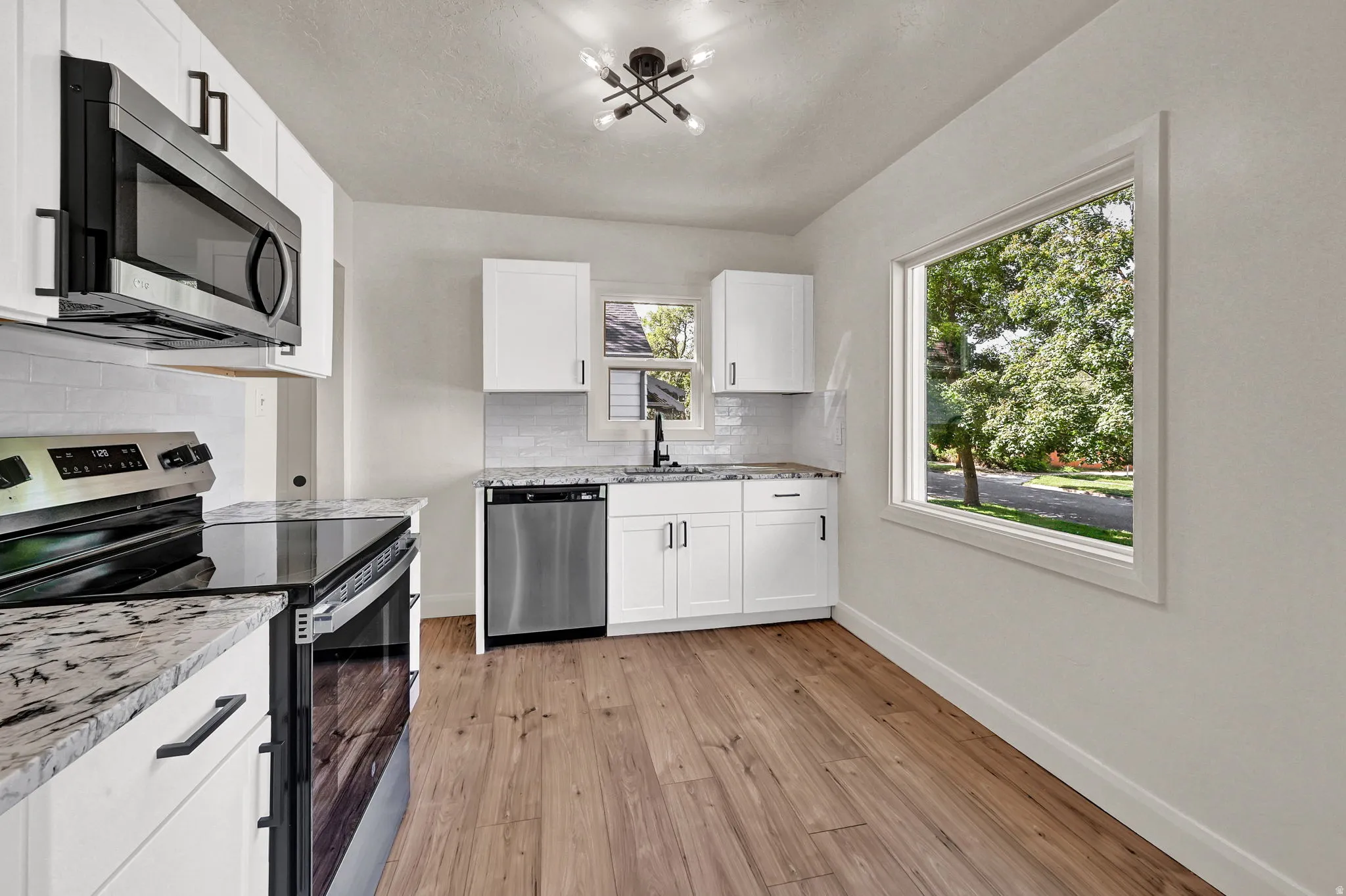 White cabinetry with black hardware, stainless steel appliances, wood-finish flooring, white subway tile backsplash, and stone countertops
