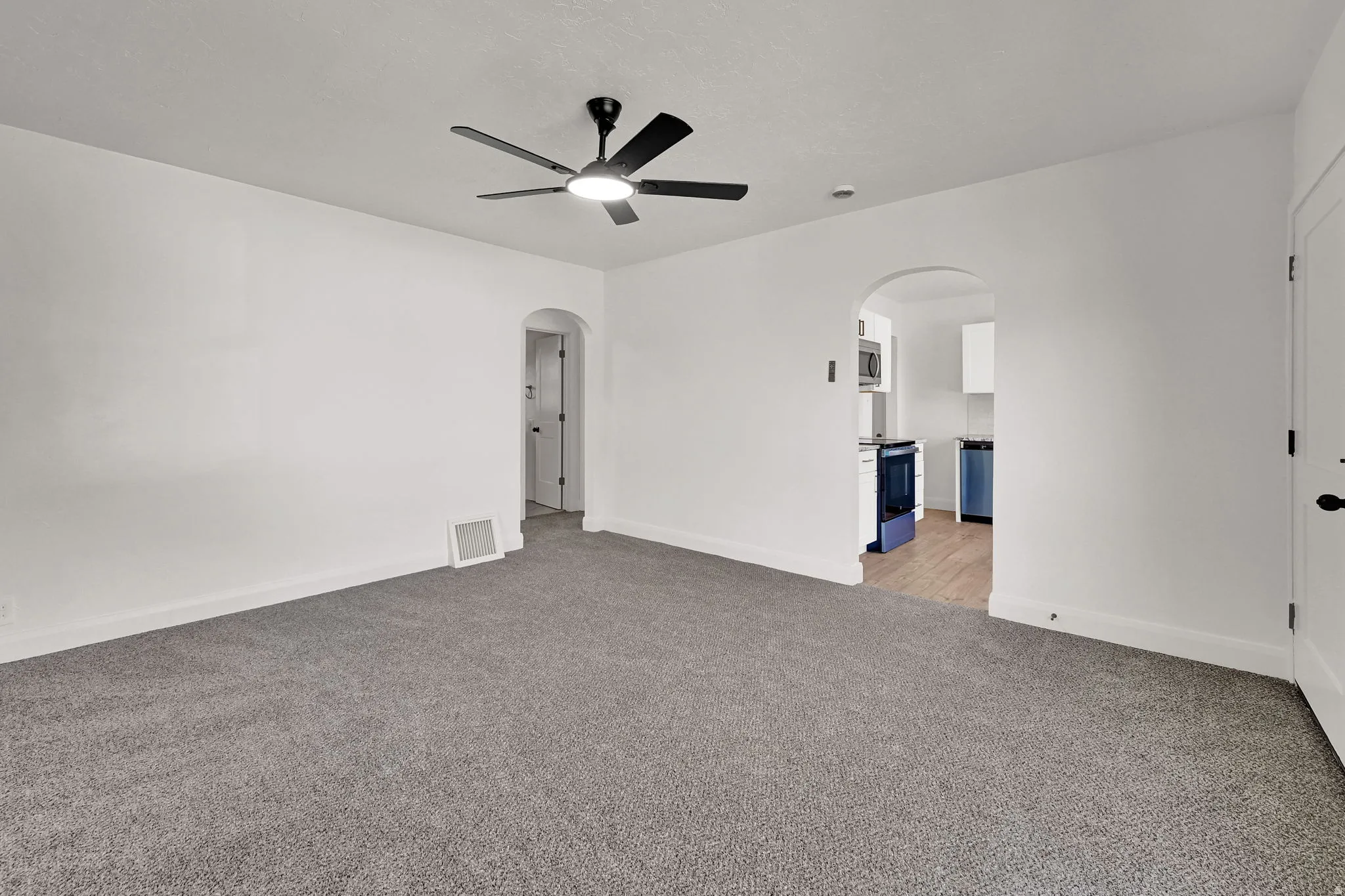 Gray carpeting, white painted walls, and a black ceiling fan with integrated lighting