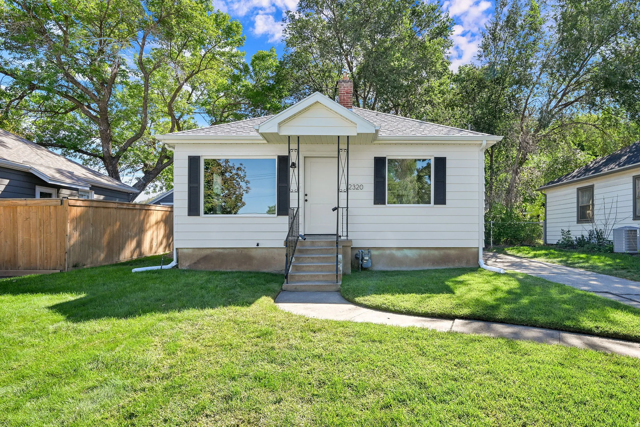 White siding exterior with a pitched roof, front entry stairs, a black wrought iron railing, and a concrete walkway