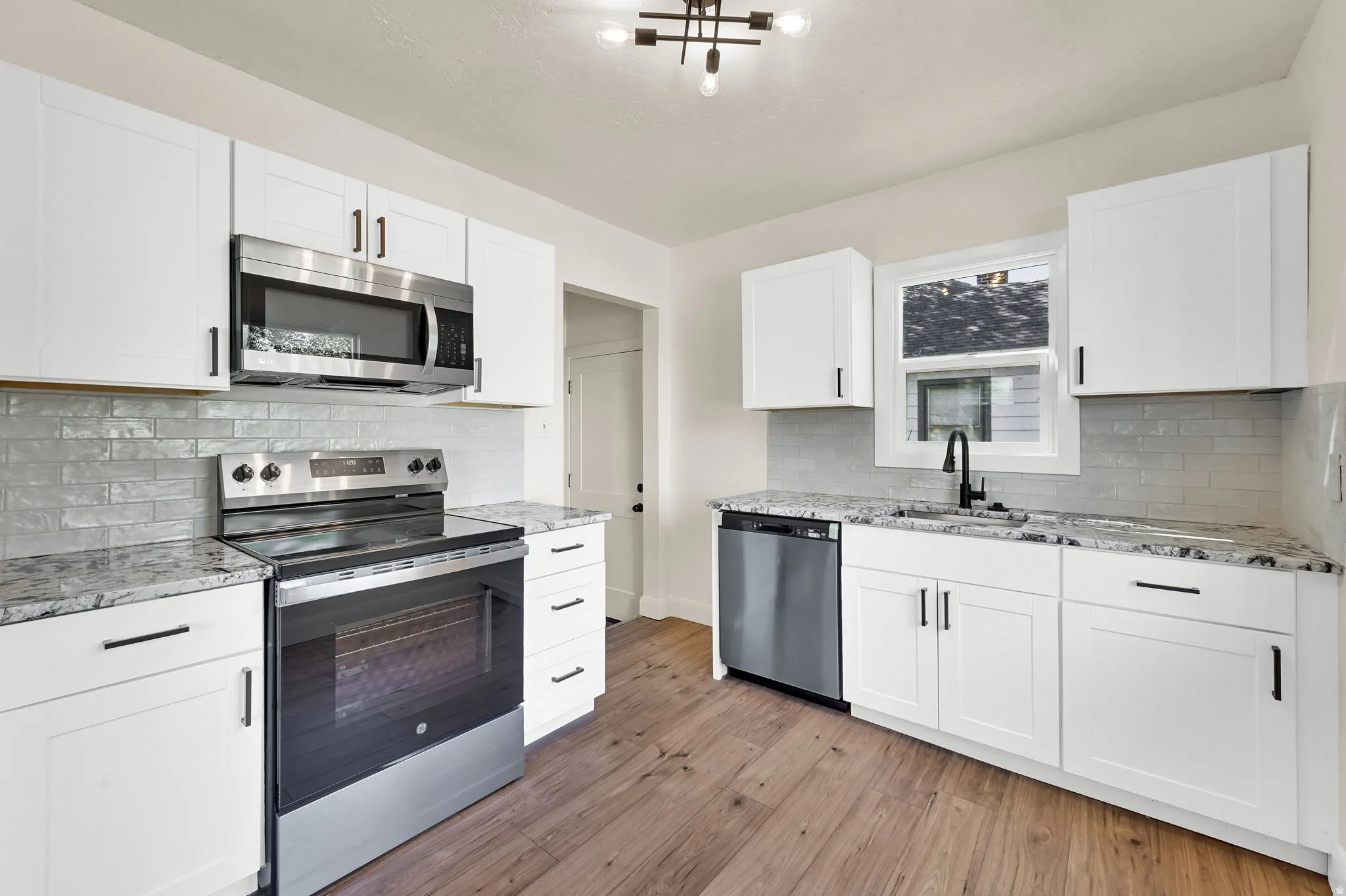 Kitchen featuring white cabinetry, stainless steel appliances, granite countertops, a subway tile backsplash, and wood-finish flooring