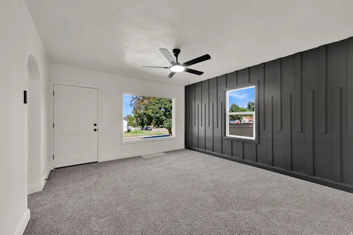 Archway entry, white paneled door, large picture window, textured accent wall, and ceiling fan with integrated lighting