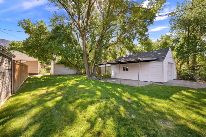 Expansive grassy yard with mature trees, a detached white garage structure, and a covered patio area
