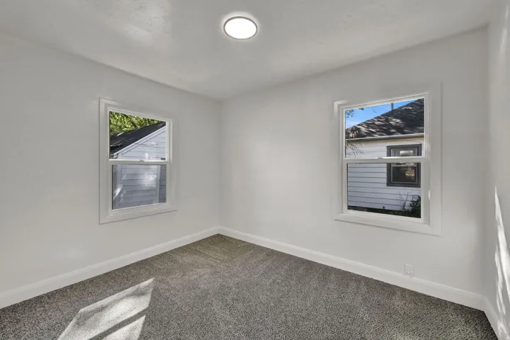 Recessed ceiling light, two windows with white trim, gray textured carpeting, and white painted walls