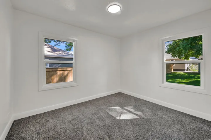 White walls, two windows with white trim, gray carpet flooring, and a flush-mount ceiling light