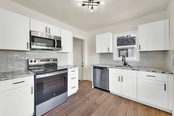 Kitchen featuring white cabinetry, stainless steel appliances, granite countertops, a subway tile backsplash, and wood-finish flooring