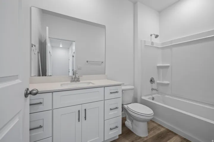Bathroom featuring a white vanity with a white countertop, chrome fixtures, a built-in tub with a shower, and wood-finish flooring