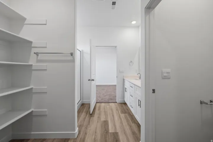 Built-in shelving, wood-finish flooring, white vanity with countertop, single basin sink, and recessed lighting
