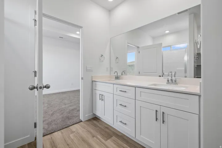 Double vanity with under-mount sinks, wood-finish flooring, and white cabinetry