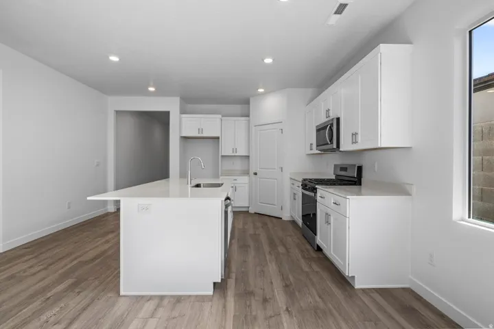 Modern kitchen featuring white cabinetry, stainless steel appliances, a center island with sink, quartz countertops, and wood-finish flooring