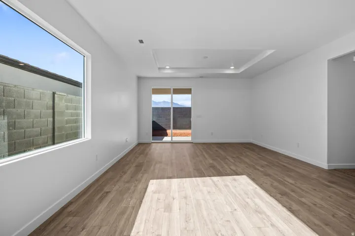 Expansive room featuring wood-finish flooring, a tray ceiling with recessed lighting, large picture window, and sliding glass door