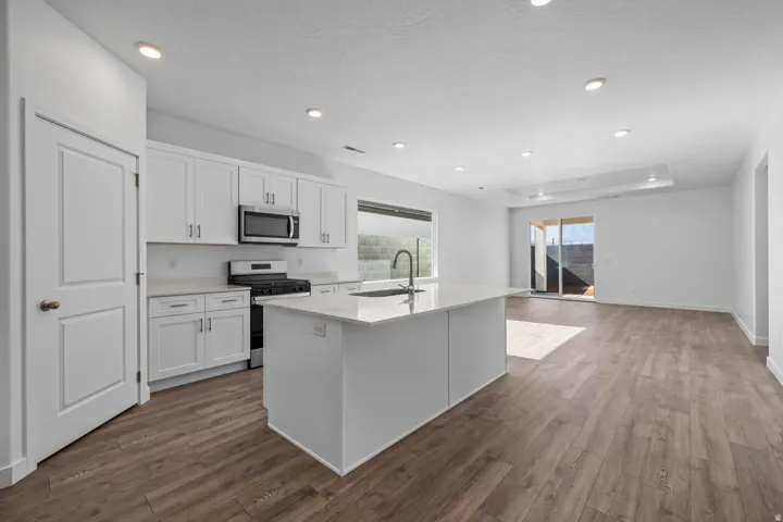 White shaker cabinetry, stainless steel appliances, central island with sink, wood-finish flooring, and recessed lighting