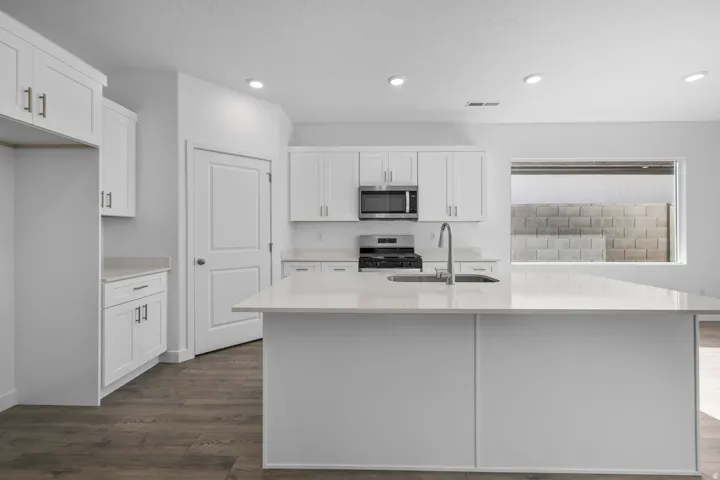 White shaker cabinetry, light-toned countertops, stainless steel appliances, wood-finish flooring, and recessed lighting