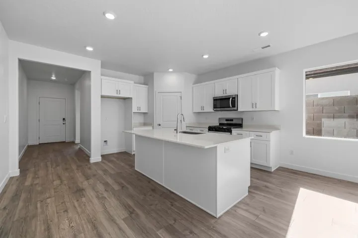 Kitchen featuring wood-finish flooring, white cabinetry, a central island with an integrated sink, and stainless steel appliances including a microwave and range