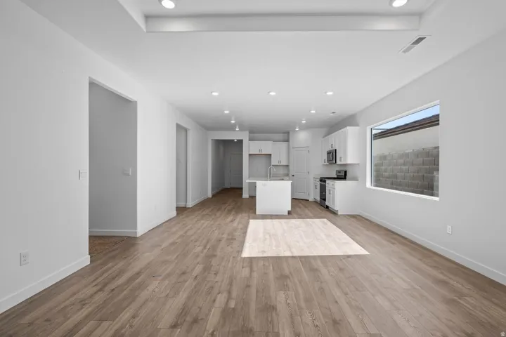 Open-concept living area featuring wood-finish flooring, recessed lighting, and a white kitchen with an island and stainless steel appliances