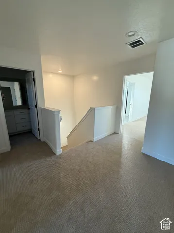 Bright upper-level landing featuring neutral carpet flooring, recessed ceiling lighting, white painted walls, and multiple doorways providing access to adjoining spaces