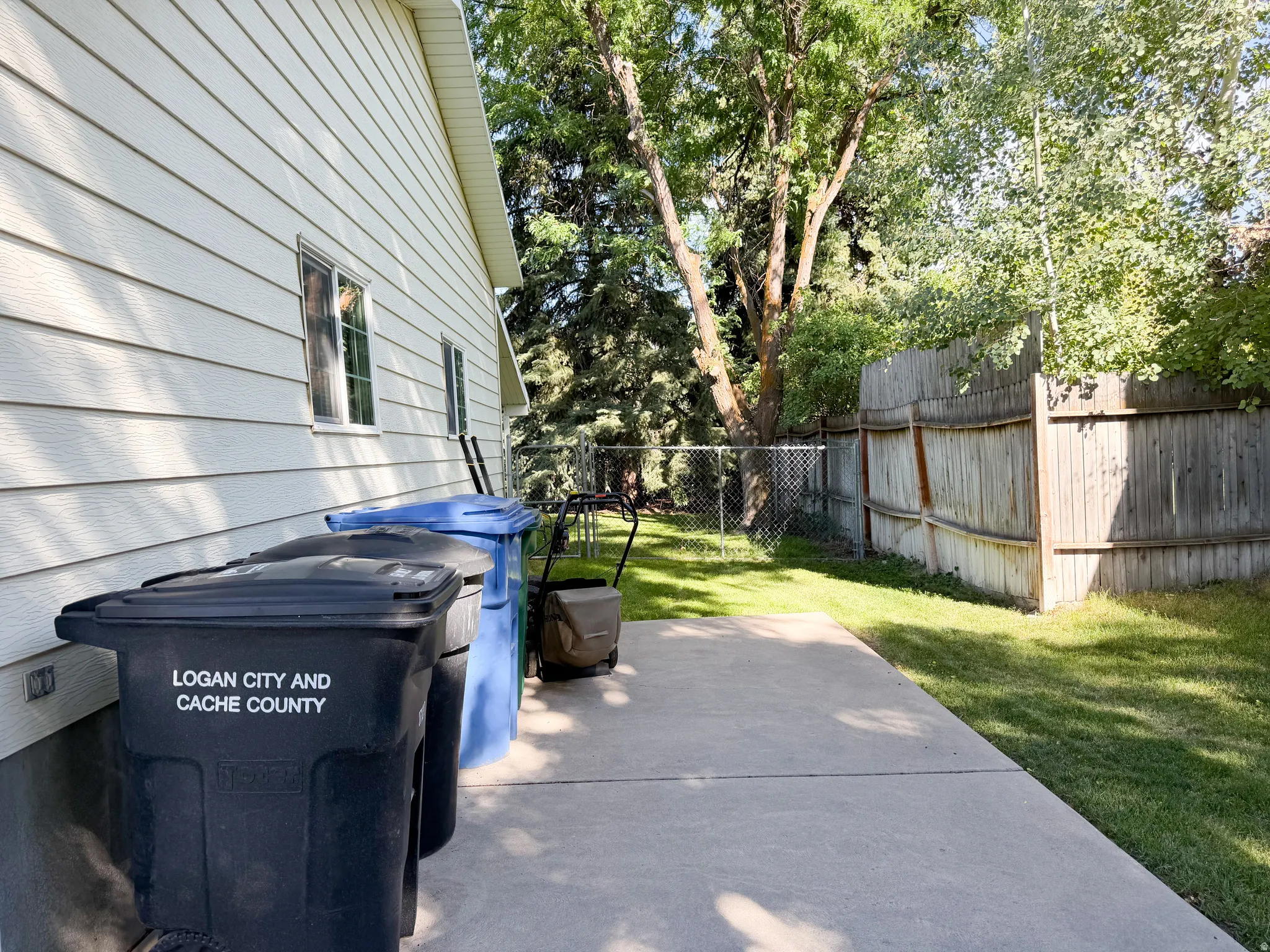 Siding exterior with multiple windows, concrete patio, grass lawn, and wood privacy fencing