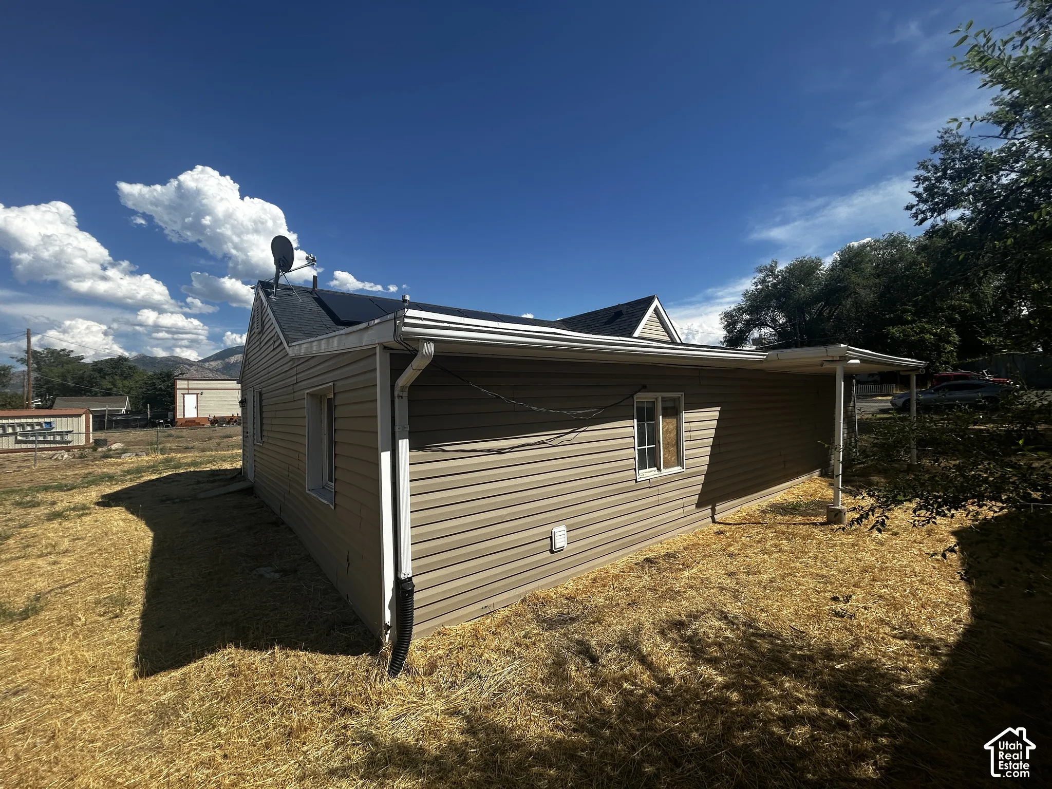 Beige siding exterior with a covered side patio, white framed windows, and a dark shingle roof