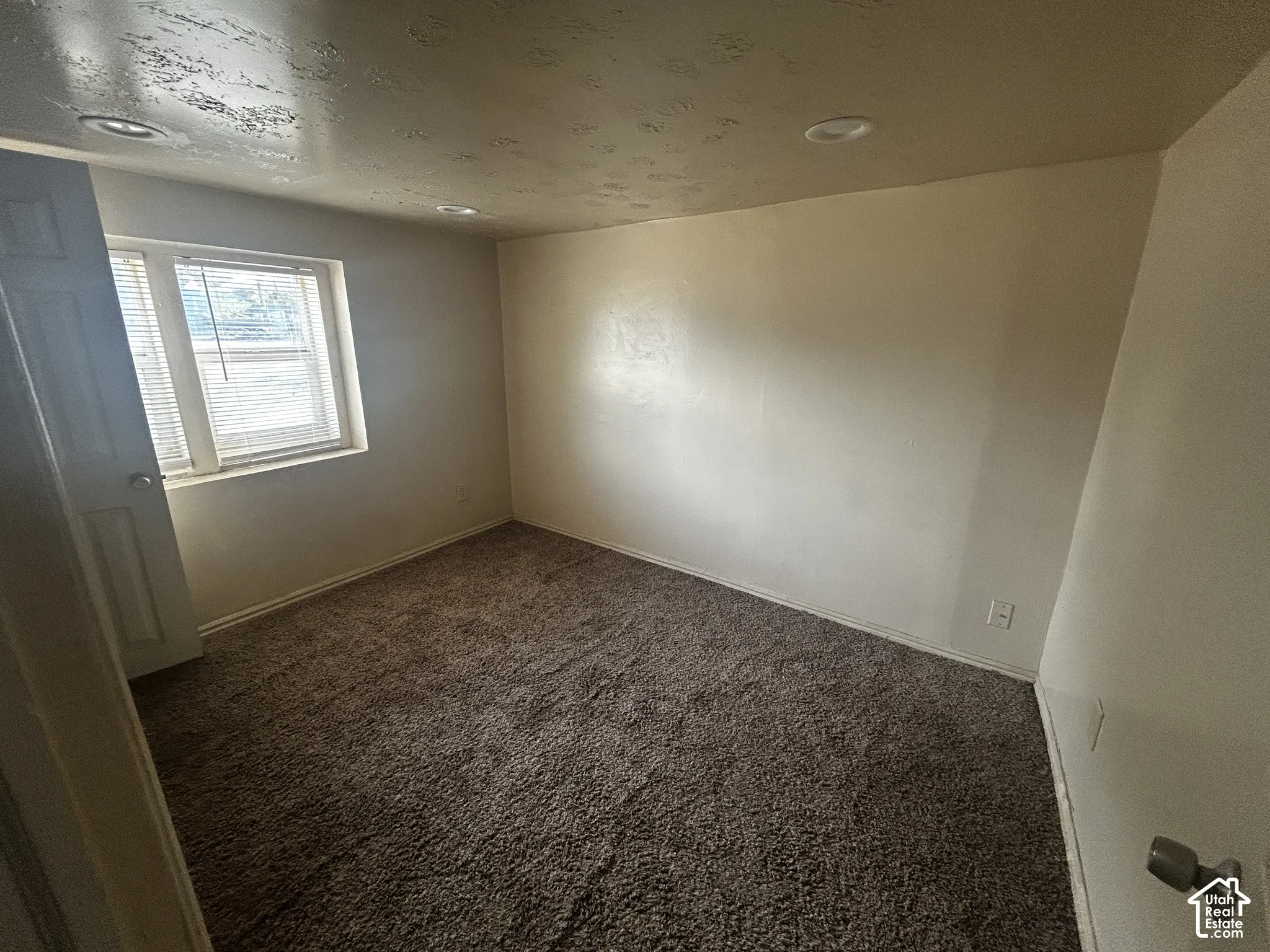 Recessed ceiling lighting, textured ceiling, light-colored walls, window with blinds, and brown carpet