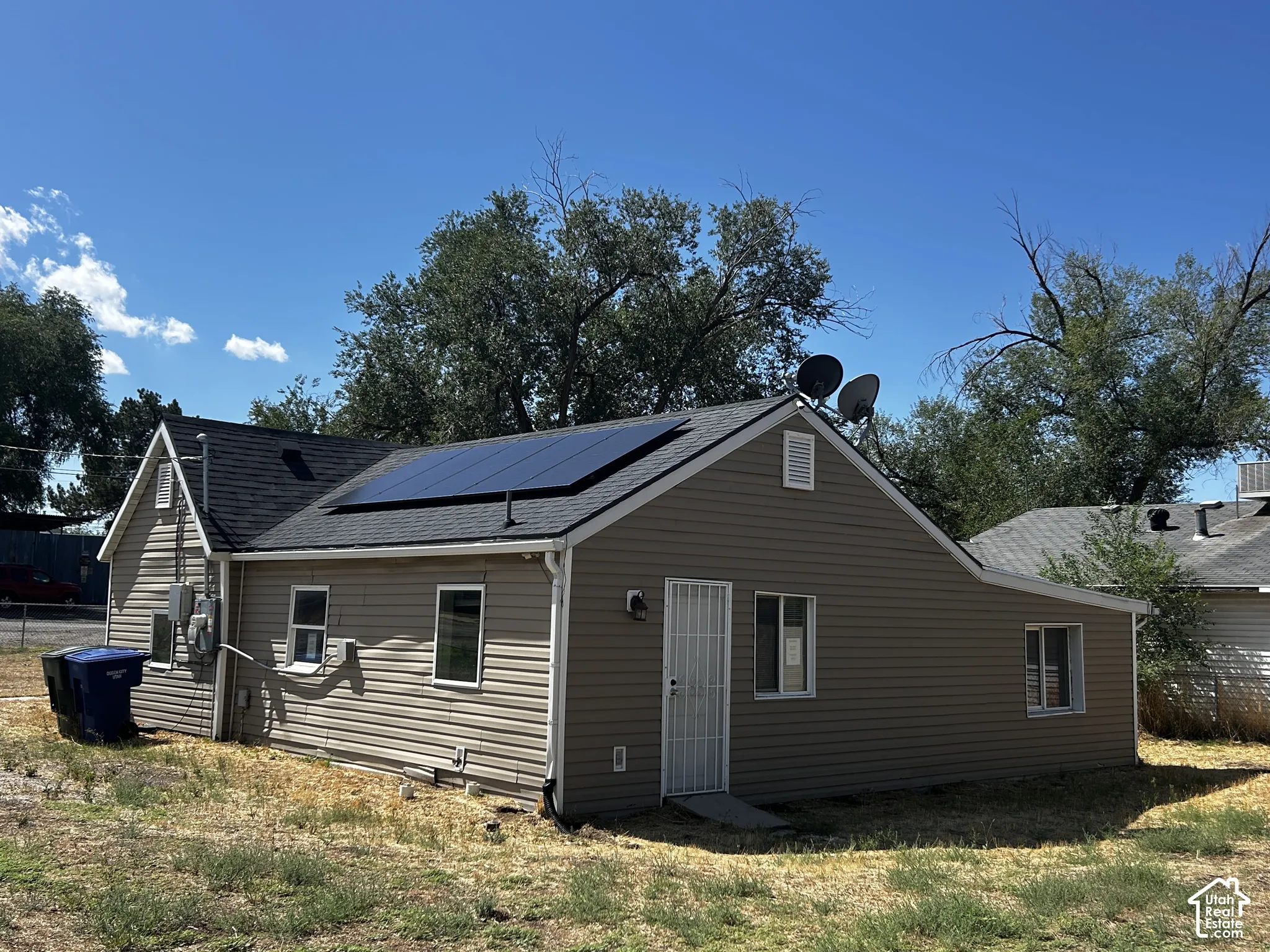 Exterior featuring solar panels, beige siding, white trim windows, and a dark shingle roof