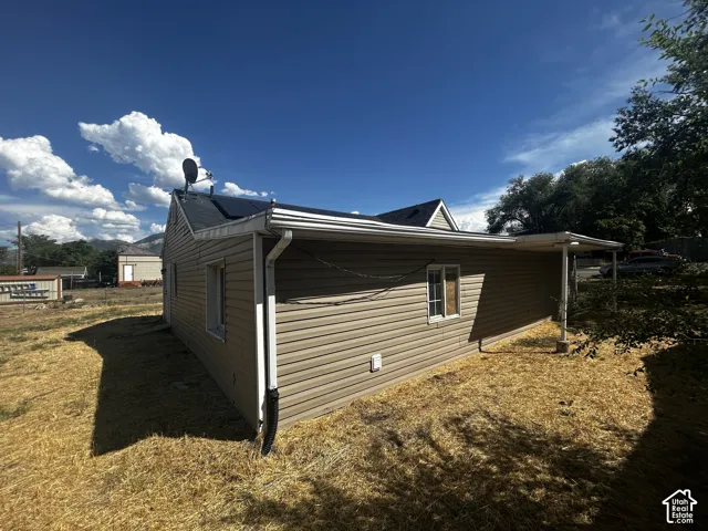 Beige siding exterior with a covered side patio, white framed windows, and a dark shingle roof